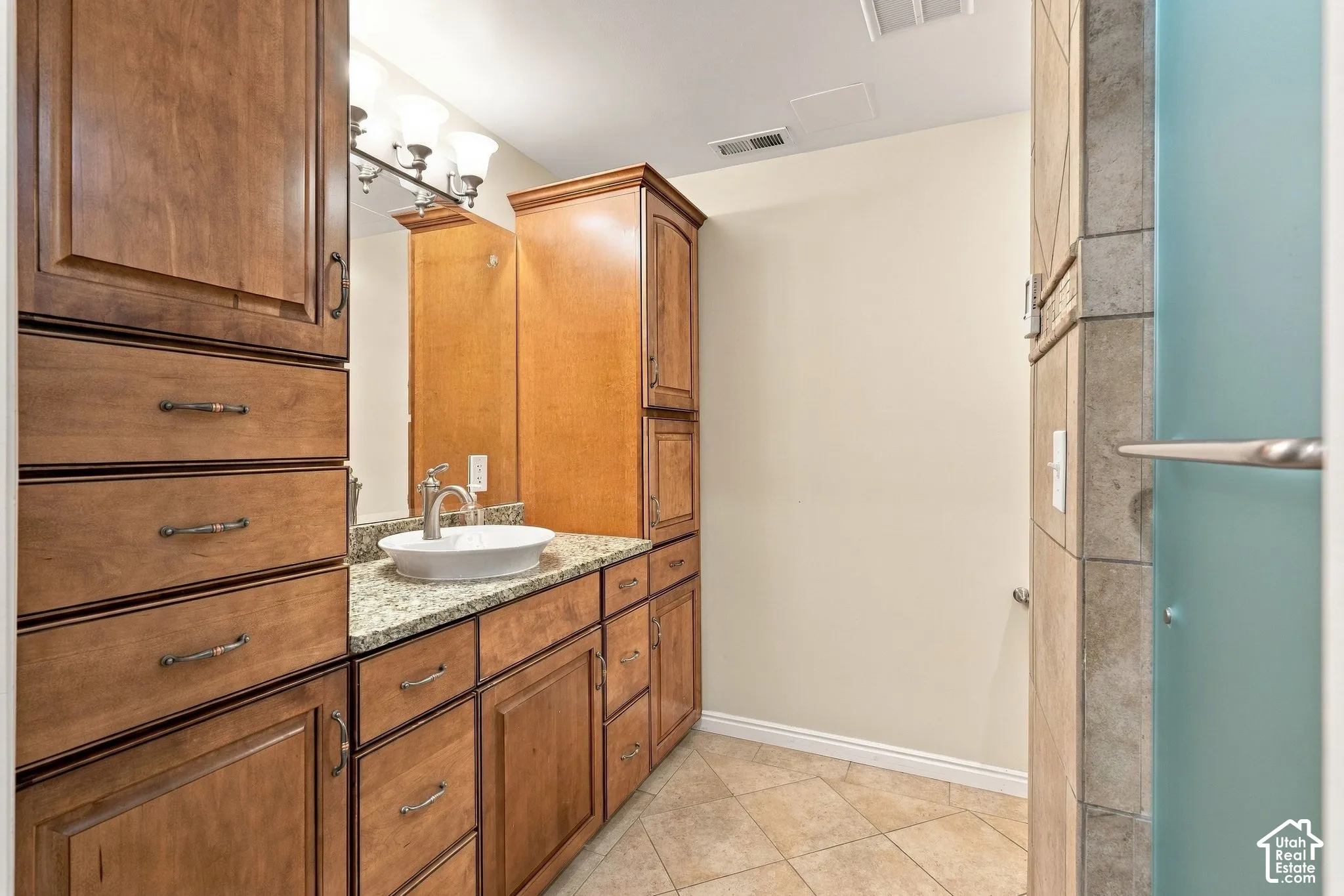 Bathroom vanity featuring custom wood cabinetry, stone countertop, vessel sink, and an integrated tall storage tower