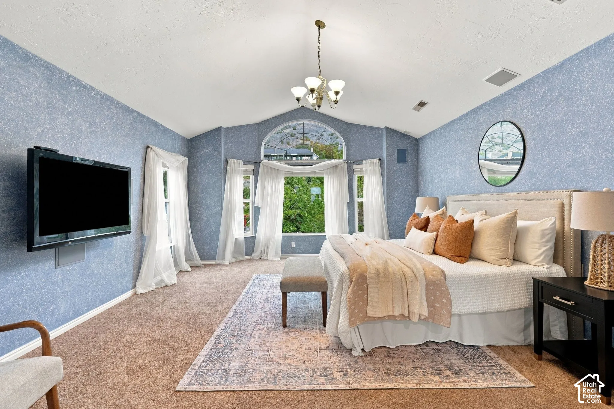 Vaulted ceilings featuring a central chandelier, expansive windows with an arched transom, and carpeted flooring