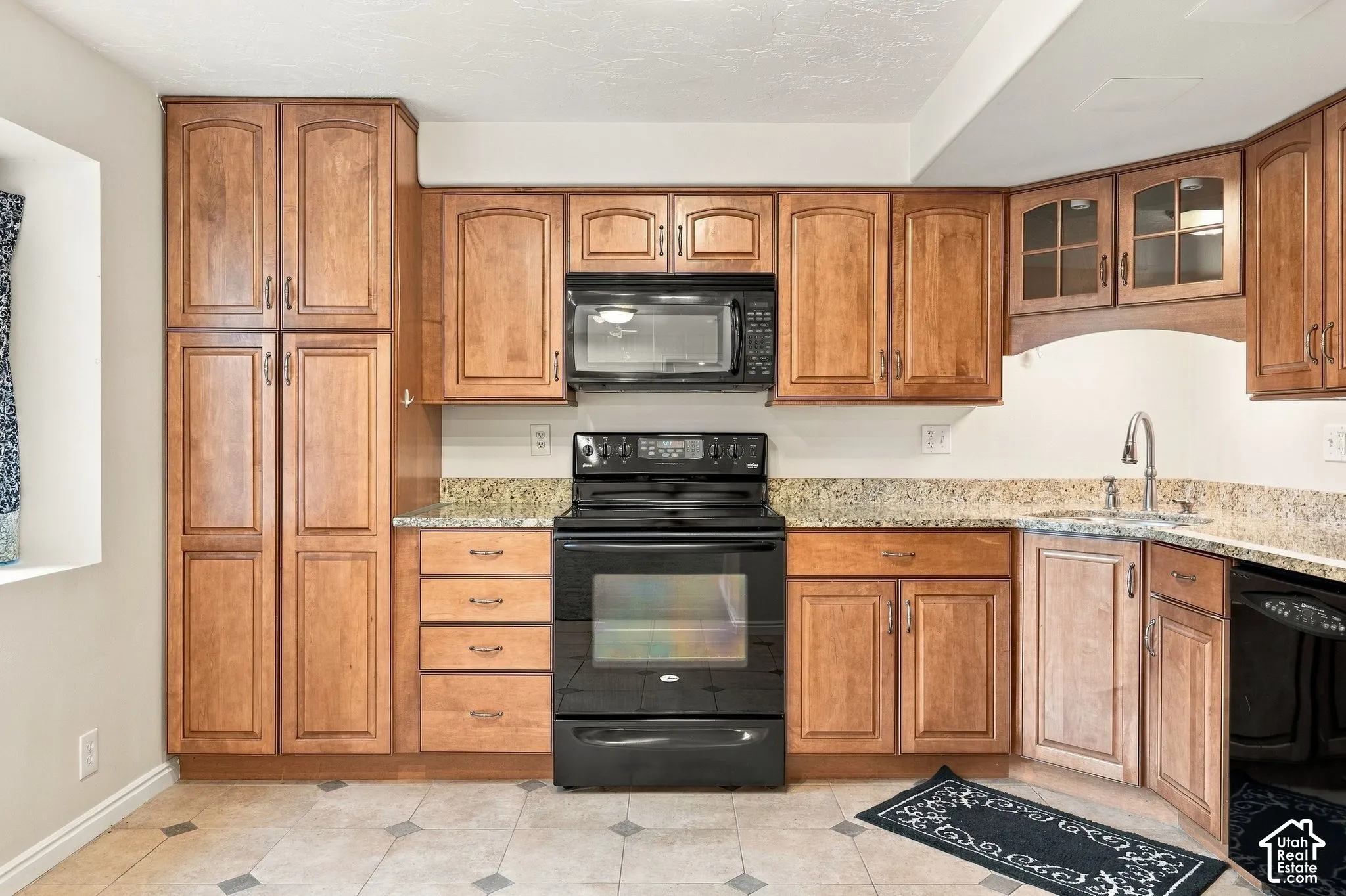Kitchen featuring warm-tone wood cabinetry, stone-surface countertops, black appliances including an over-the-range microwave, and tile flooring