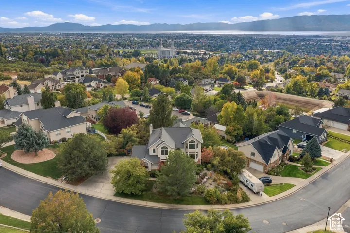 Aerial perspective of a hillside residential neighborhood featuring expansive mountain range backdrops, mature trees, multi-level residential architecture, paved cul-de-sac streets, and panoramic valley terrain