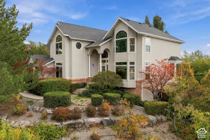 Multi-level exterior featuring stucco and brick masonry, arched entryway, bay windows, and tiered stone landscaping