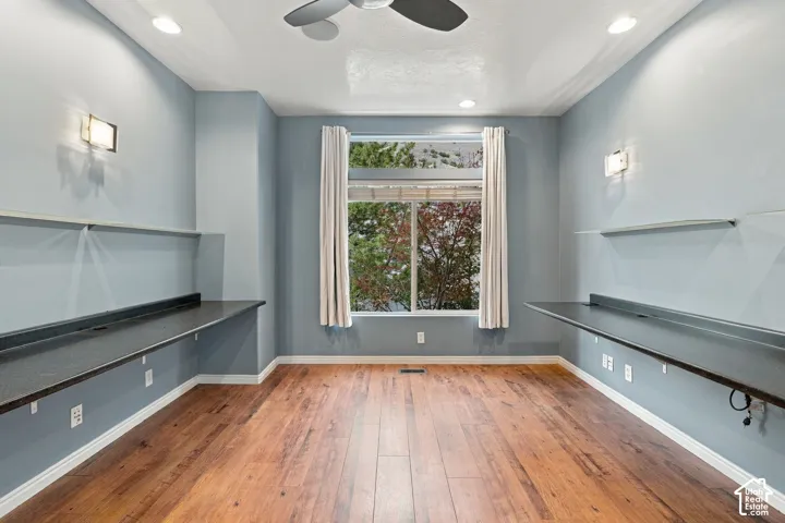Room featuring wood-finish flooring, dual built-in desks with stone-style surfaces, recessed lighting, and a window with a natural backdrop