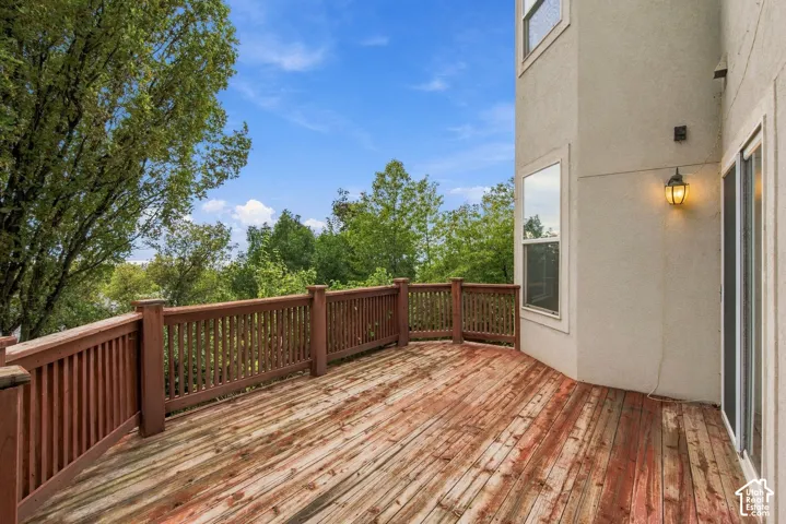 Elevated deck featuring wooden plank flooring, wooden railing, and wall-mounted exterior lighting