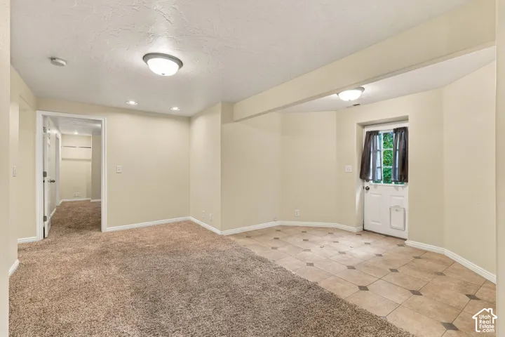Room featuring a combination of wall-to-wall carpeting and tile flooring with decorative inserts, flush-mount ceiling lighting, and a door providing exterior access