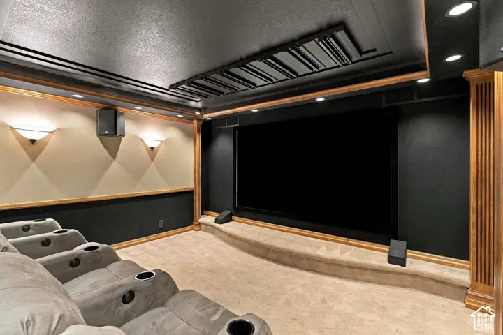 Dedicated theater room featuring a tiered platform, recessed ceiling lighting, wall-mounted light fixtures, dark decorative wall paneling, and wood-trim accents