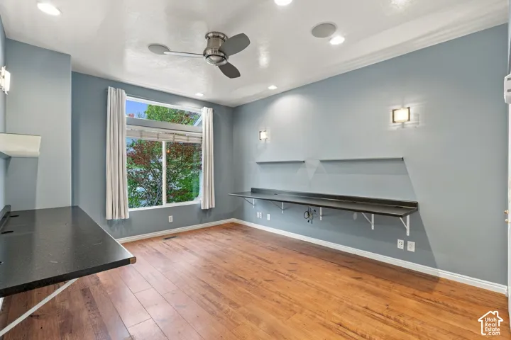 Room featuring wood-finish flooring, recessed lighting, a ceiling fan, dual wall-mounted desks with integrated shelving, and large windows