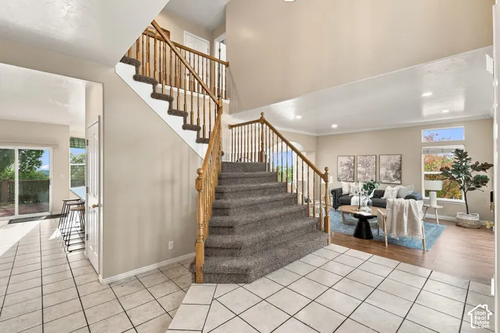 Grand foyer featuring a staircase with carpeted treads and natural wood-finish railings, high ceilings, recessed lighting, and tile flooring