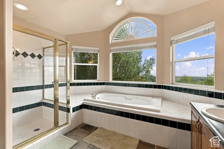 Ensuite bathroom featuring a recessed soaking tub, glass-enclosed shower, vaulted ceiling with integrated lighting, and multiple windows including an arched transom window