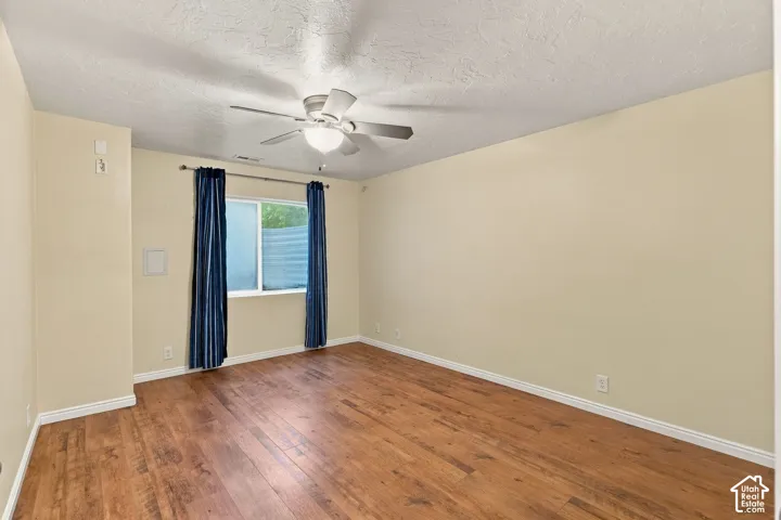 Room featuring wood-finish flooring, a neutral wall palette, and a multi-blade ceiling fan with integrated lighting