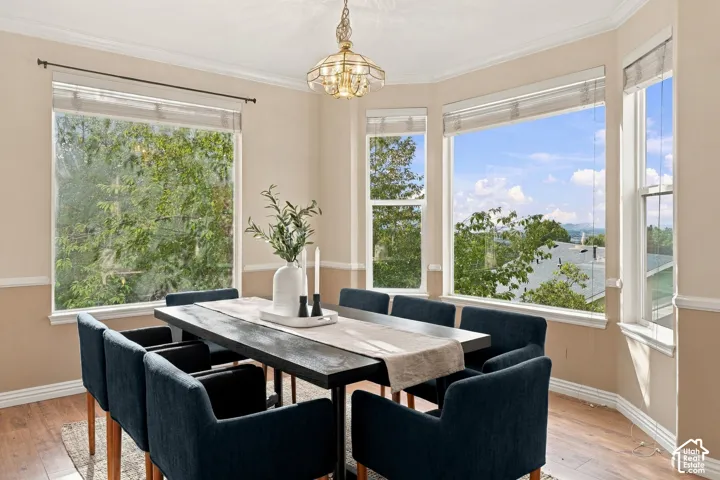Bay window featuring multiple expansive panes, crown molding, chair rail trim, wood-finish flooring, and a tiered metal chandelier