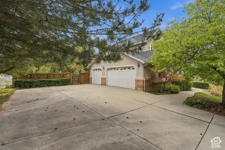 Concrete driveway with a three-car garage, brick foundation detailing, and wood perimeter fencing