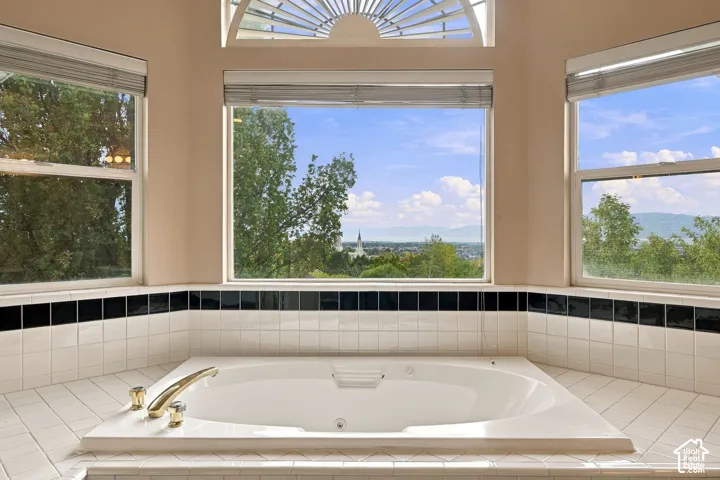 Built-in soaking tub with gold-tone fixtures, tile surround featuring black accent detailing, and expansive windows with arched transom overhead
