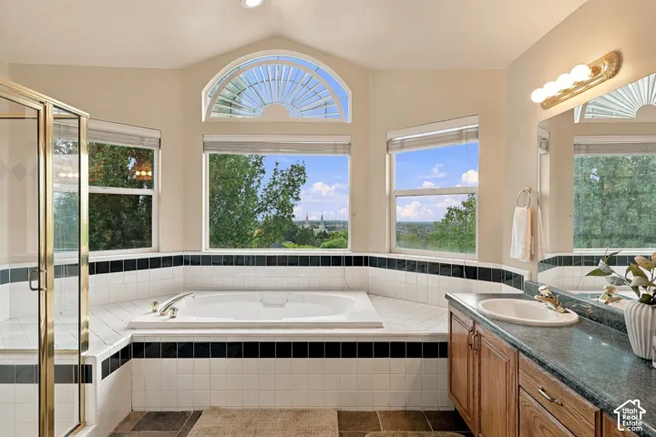 Bathroom featuring a soaking tub, arched window, glass-enclosed shower, wood-finish cabinetry, and stone-surface countertop