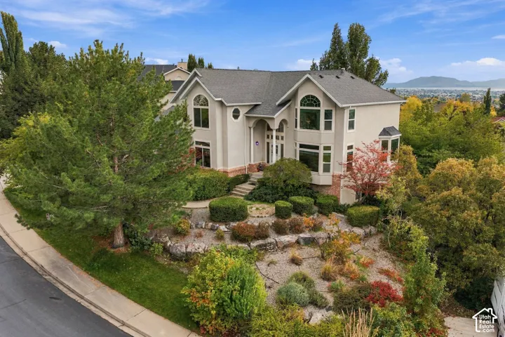 Two-story residence featuring a multi-gabled roofline, arched window detailing, stone retaining walls, tiered landscaping, and an attached multi-car garage