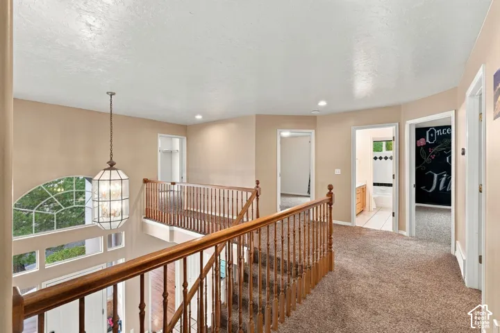 Open landing featuring wood-finish railings, recessed lighting, carpeted flooring, and a multi-panel decorative pendant fixture