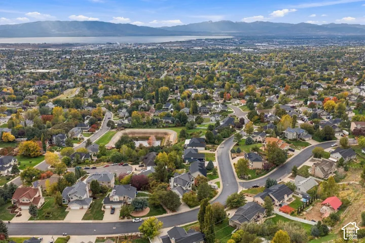 Aerial perspective showcasing a hillside residential setting featuring mature landscaping, paved roadways, a retained detention basin, and a panoramic mountain and lake backdrop