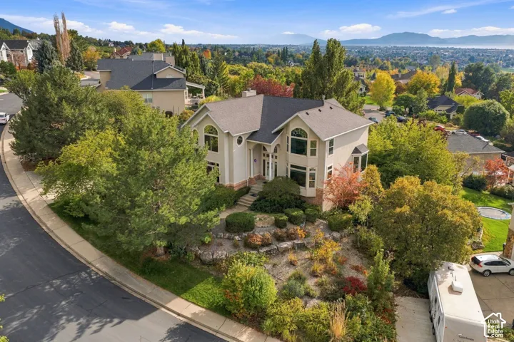 Two-story residence featuring light-toned stucco siding, an asphalt shingle roof, multi-pane arched windows, and landscaped terraced grounds with mature trees