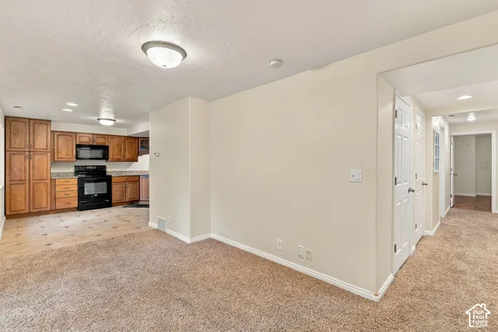 Kitchen featuring wood cabinetry, stone-finish countertops, and built-in black appliances, set against wall-to-wall carpeting and neutral wall tones