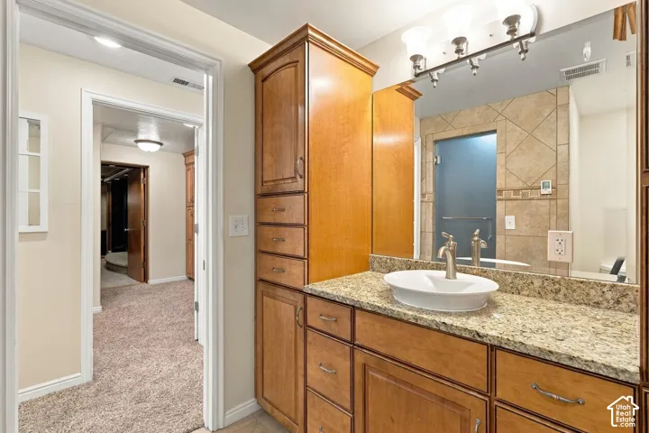Bathroom vanity featuring wood cabinetry, stone-surface countertop, oval vessel sink, and an integrated full-height linen tower
