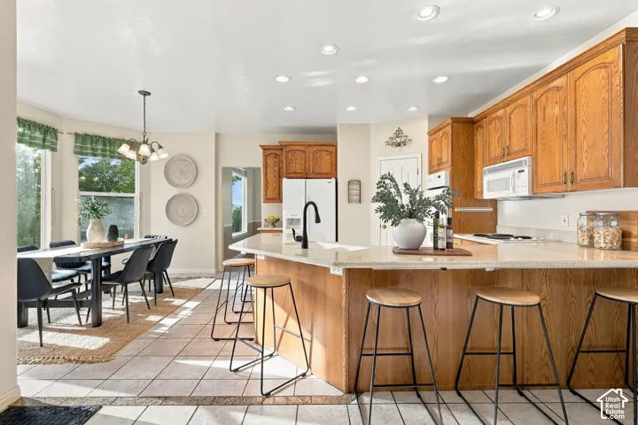 Kitchen featuring wood cabinetry, stone-surface breakfast bar, matte black faucet, recessed lighting, and tile flooring