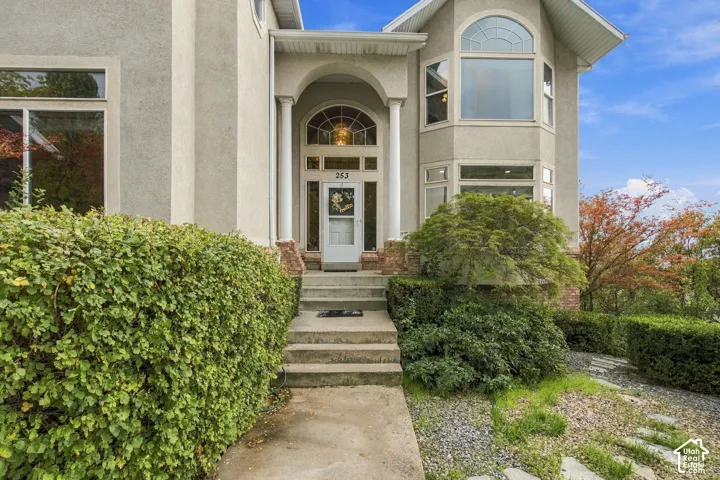Stucco exterior featuring an arched entryway with decorative columns, a glass-panel door with transom and side light windows, and a multi-level bay window configuration