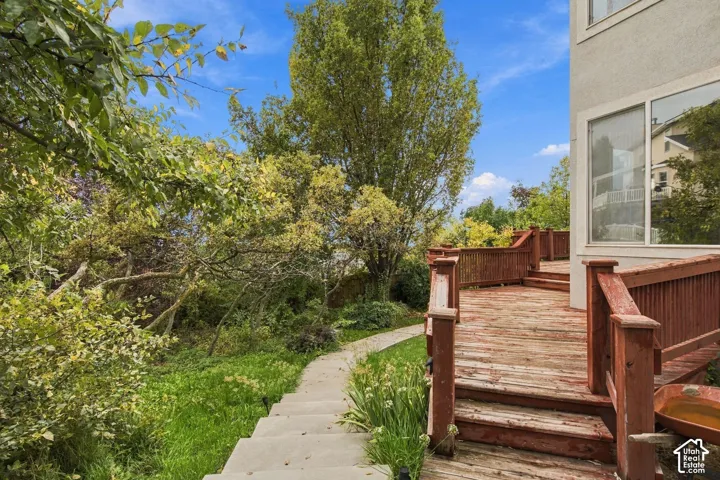 Multi-level wood deck featuring built-in railings, concrete stairs, mature trees, and landscaped greenery