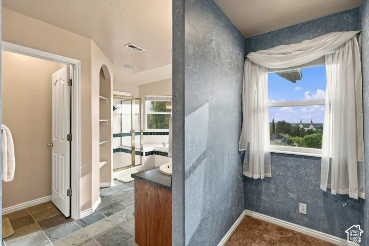 Bathroom featuring natural stone tile flooring, built-in recessed shelving, a glass-enclosed shower, and a vanity with a stone countertop