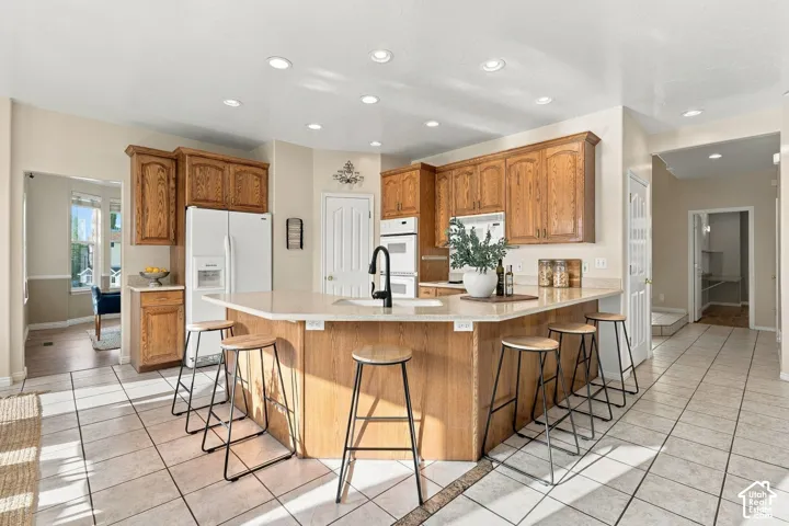 Kitchen featuring wood cabinetry, solid-surface countertops, a center island with a prep sink, recessed ceiling lighting, and tile flooring
