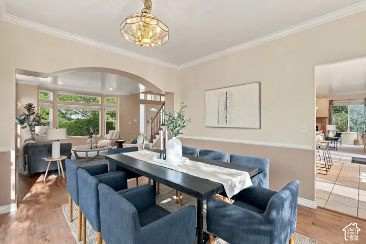 Dining area featuring wood-finish flooring, a decorative pendant light fixture, arched architectural detailing, and crown molding