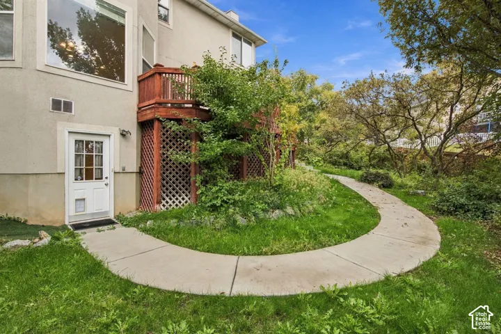 Exterior featuring a raised wood deck with lattice skirting, a curved concrete walkway, and landscaped grounds with mature trees