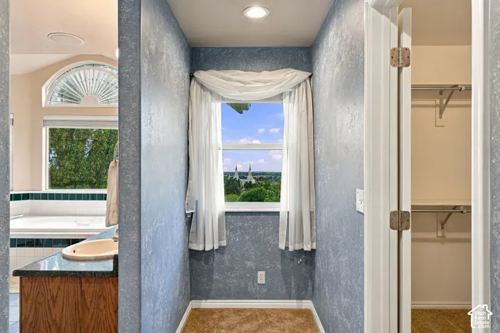 Built-in vanity featuring a dark stone countertop with integrated basin, recessed lighting, arched window with fanlight detailing, and walk-in closet with overhead shelving