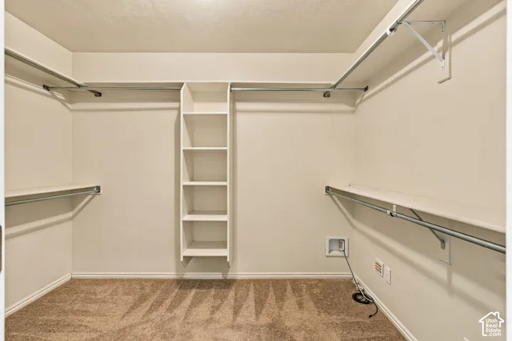 Walk-in closet featuring wall-to-wall carpet, built-in shelving tower, and tiered metal garment rods