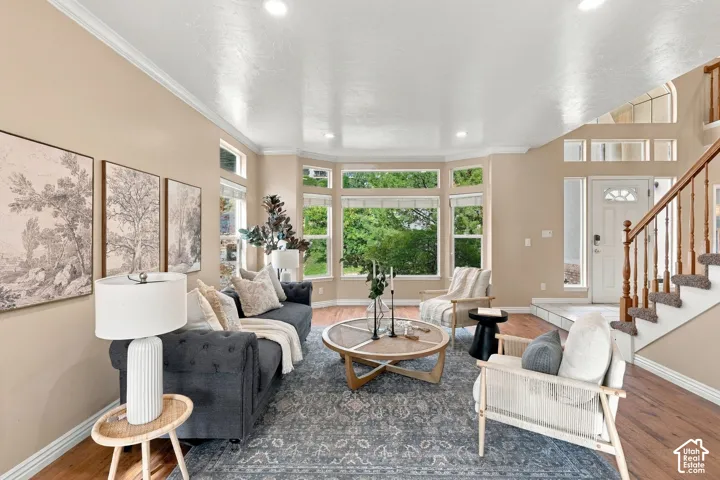 Open-concept area featuring wood-finish flooring, a multi-paneled bay window, recessed ceiling lighting, and a staircase with a wooden balustrade