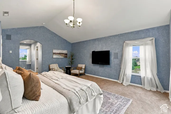 Vaulted ceiling featuring a central multi-arm chandelier, textured wall finishes, arched entry, and window treatments