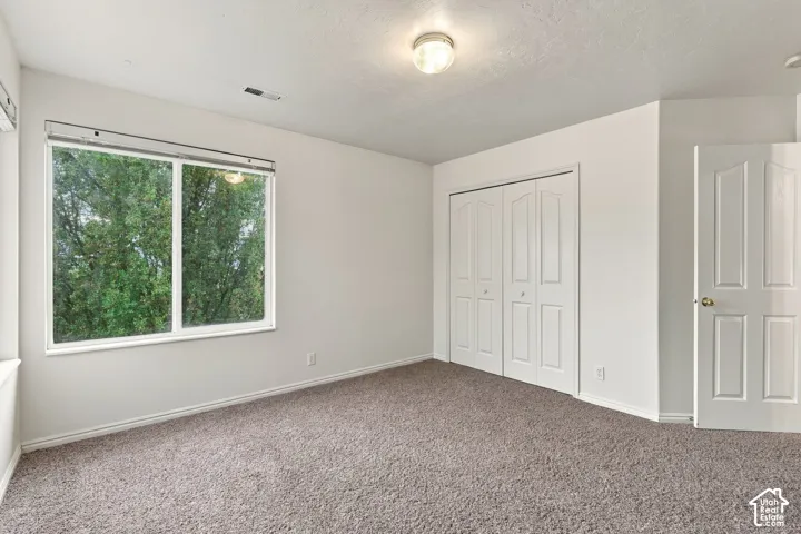 Room featuring neutral wall-to-wall carpeting, a dual-panel sliding closet, a white four-panel interior door, and a single-pane window