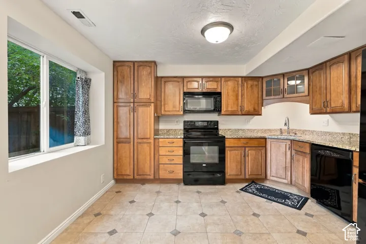 Kitchen featuring natural wood cabinetry, stone-finish countertops, black built-in appliances, large window, and tile flooring