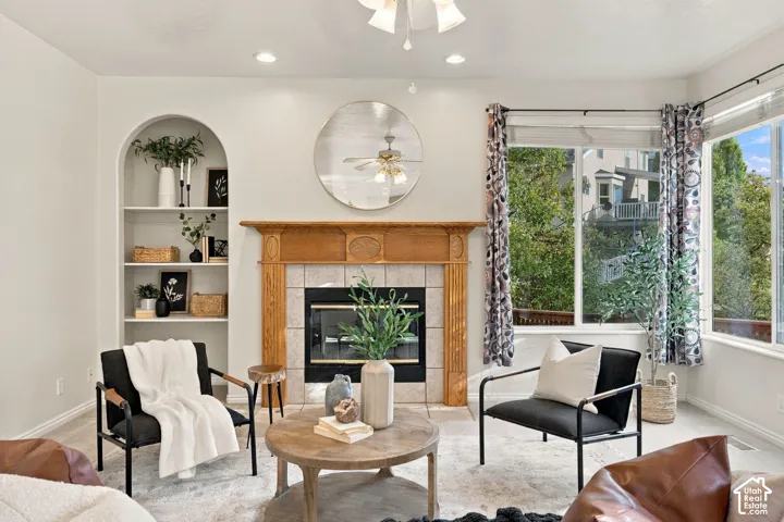 Fireplace featuring a decorative oak mantel and neutral tile surround, built-in arched display shelving, and large windows with natural light