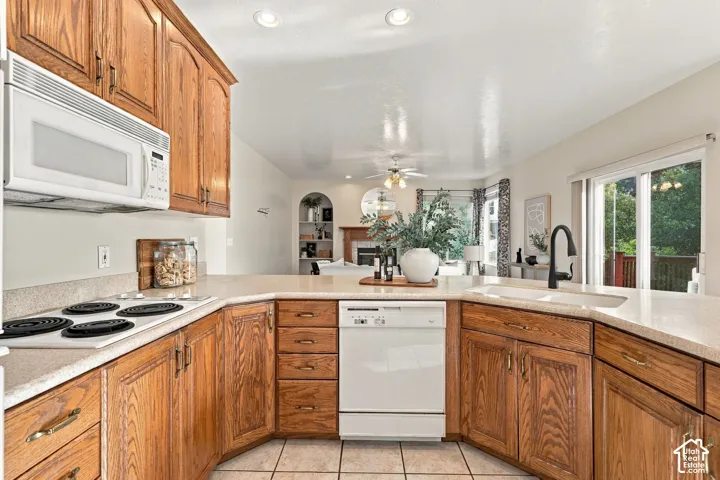 Kitchen featuring wood cabinetry, stone-finish countertops, ceramic tile flooring, and integrated white appliances including a built-in microwave and dishwasher