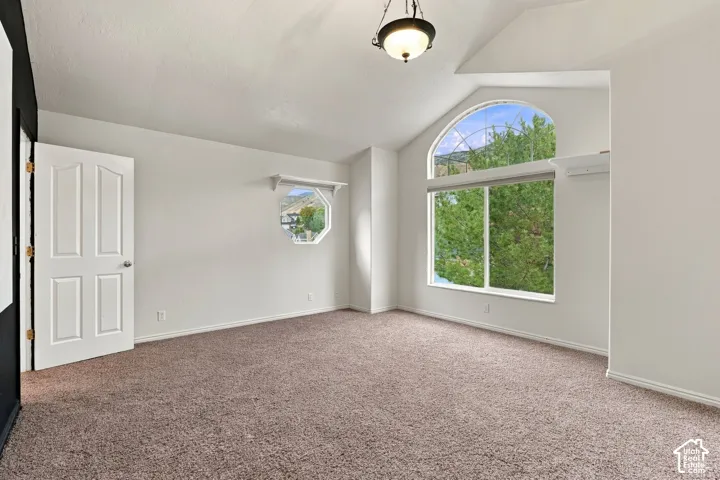 Vaulted ceilings, large arched window, octagonal accent window, carpeted flooring, and a central pendant light fixture