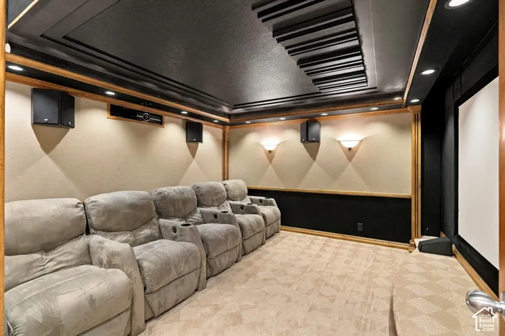 Dedicated media room featuring a coffered ceiling with acoustic paneling, tiered platform flooring, wall-mounted speakers, and integrated recessed lighting