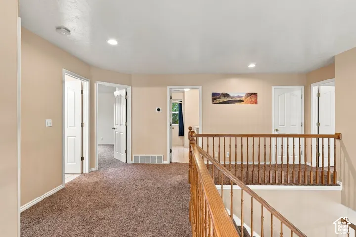 Open landing featuring neutral wall tones, wall-to-wall carpeting, wood-finish balustrade with decorative spindles, and multiple interior paneled doors