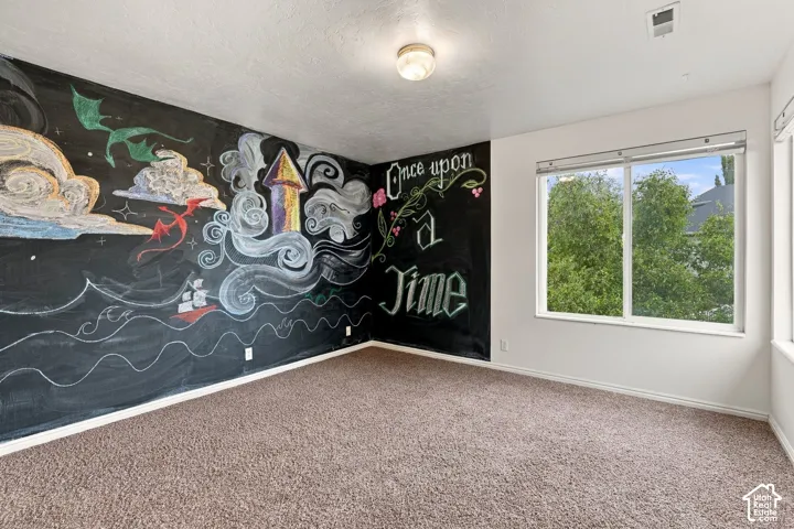 Room featuring carpeting, a large window, a decorative chalkboard accent wall, and a flush-mount light fixture