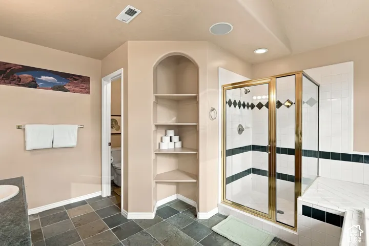 Bathroom featuring natural slate floor tiling, a walk-in shower with gold-finish frame, decorative tile inlay, integrated corner shelving, and recessed ceiling lighting