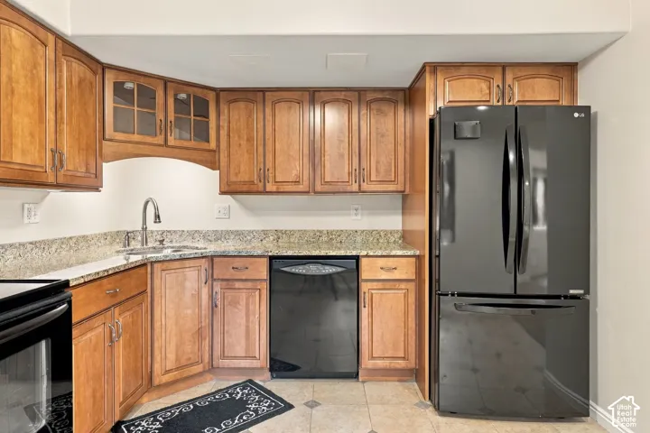 Kitchen featuring wood cabinetry, stone countertops, tiled flooring, and black appliances