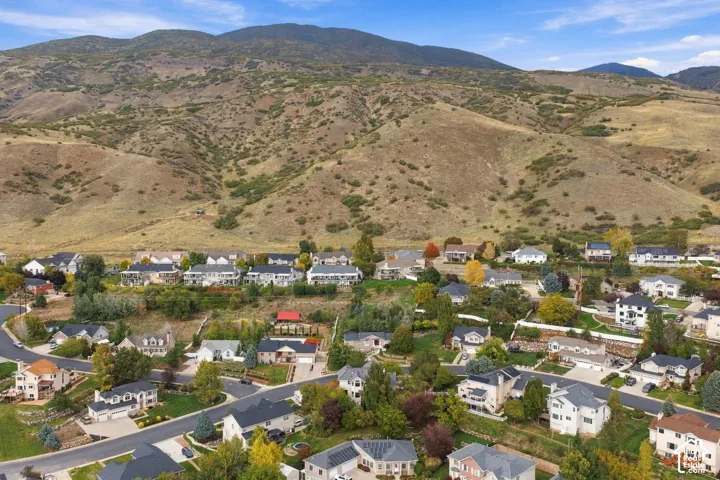 Aerial perspective featuring a neighborhood landscape backdropped by expansive mountain ranges, mature trees, and paved street infrastructure