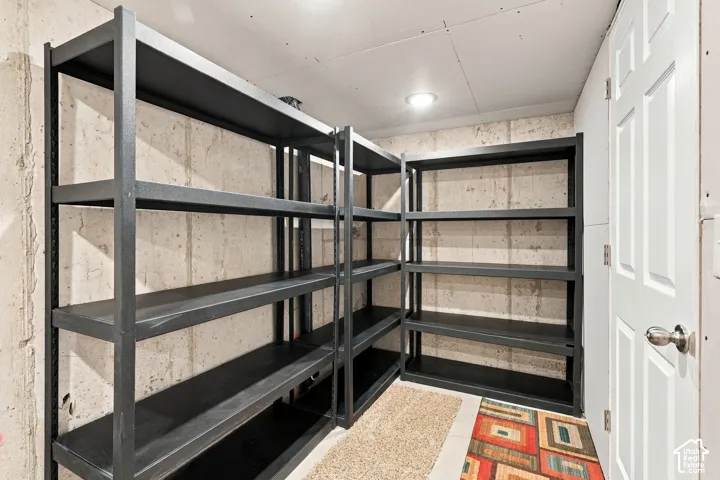 Storage space featuring exposed concrete walls, recessed ceiling lighting, and a paneled interior door