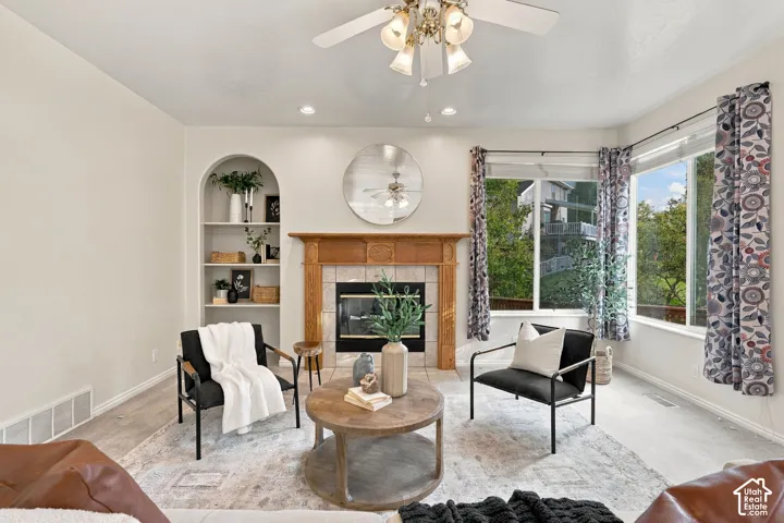 Living area featuring a fireplace with a wood mantel, tile surround, integrated arched shelving, wood-finish flooring, and a multi-light ceiling fan