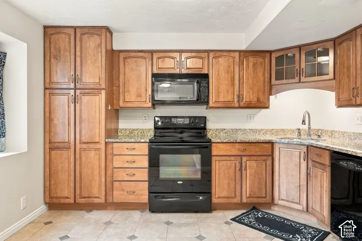 Kitchen featuring warm-tone wood cabinetry, stone-surface countertops, black appliances including an over-the-range microwave, and tile flooring