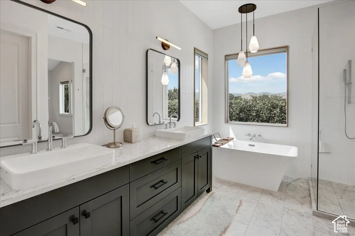Dual vanity with vessel sinks, a freestanding soaking tub, a walk-in shower with glass enclosure, and a multi-pendant light fixture