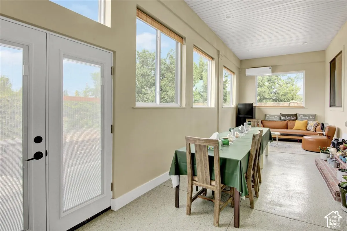 Spacious sunroom featuring multiple large windows, French doors, a built-in air conditioning unit, and a durable speckled flooring